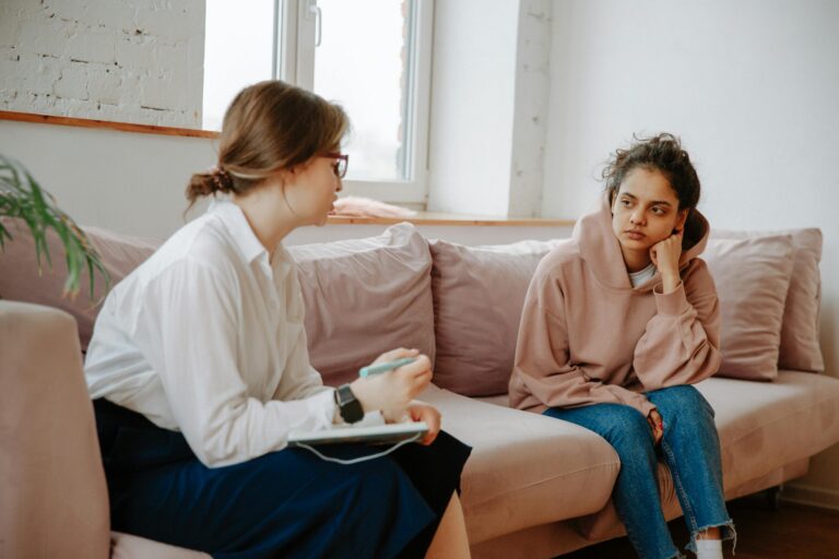A teenager in a hoodie having a therapy session with a female therapist on a sofa.