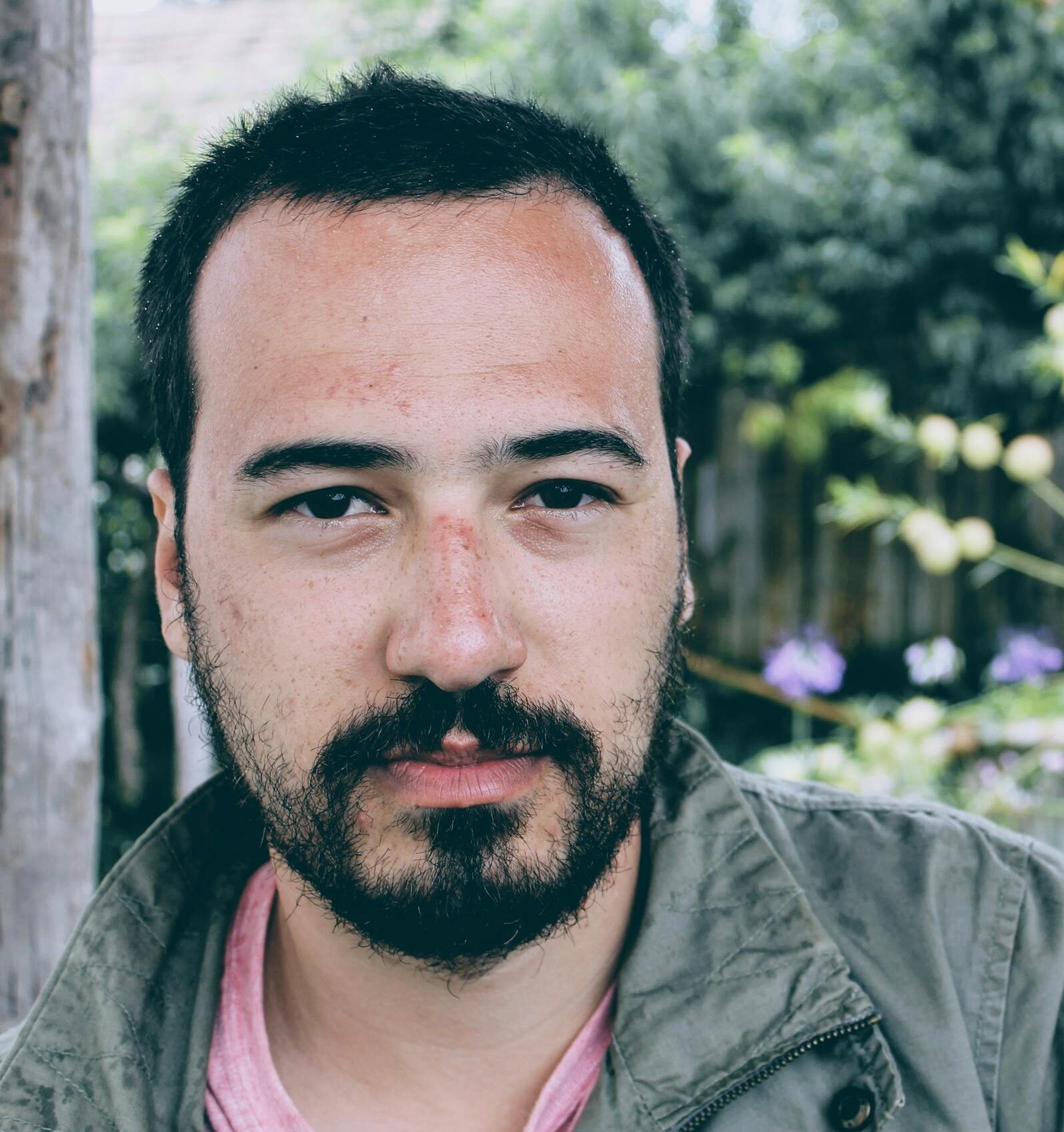 Portrait of a young man with facial hair, outdoors in a natural setting. Serious expression.